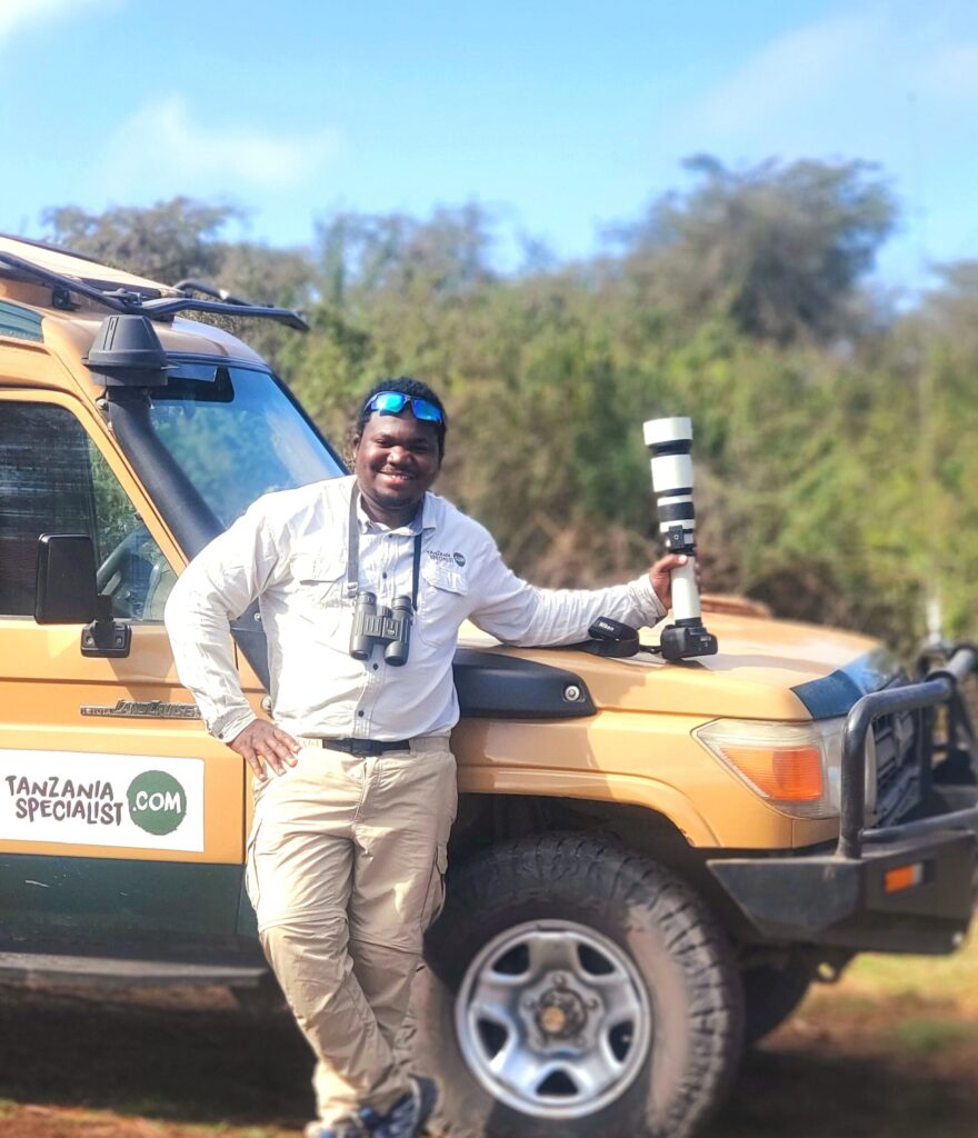 Reiseekspert i Tanzania, Laizer, står foran en jeep.