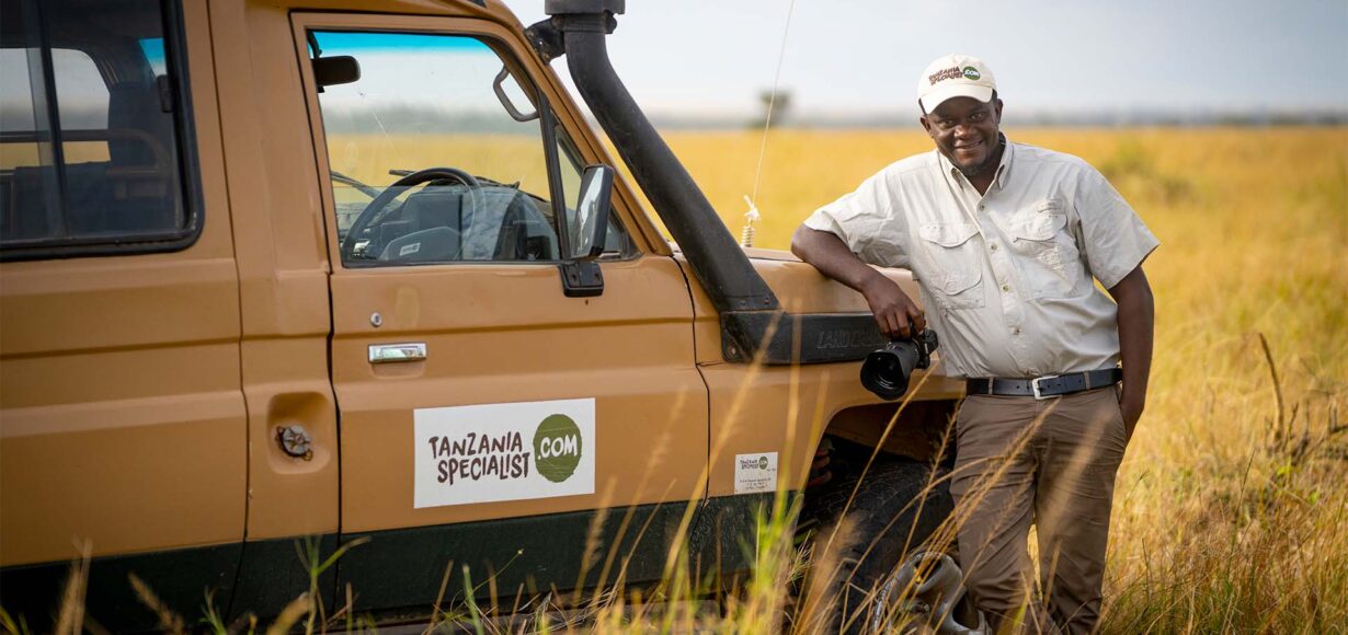 ferie i Tanzania. Guide lener seg på jeep fra Tanzania Specialist.