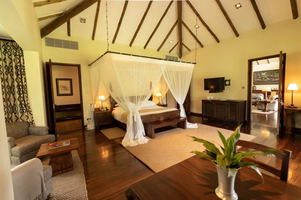 Arusha lodge, rom med treseng med myggnetting, grå stoler og et lyst teppe
