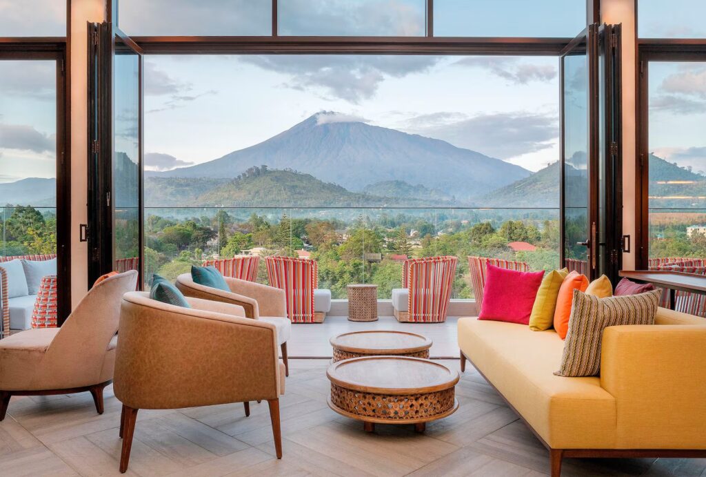 Gran Melia lodge i Arusha, lounge med lyse lenestoler, en gul sofa, åpne dører til terrasen og Mount Meru i bakgrunnen