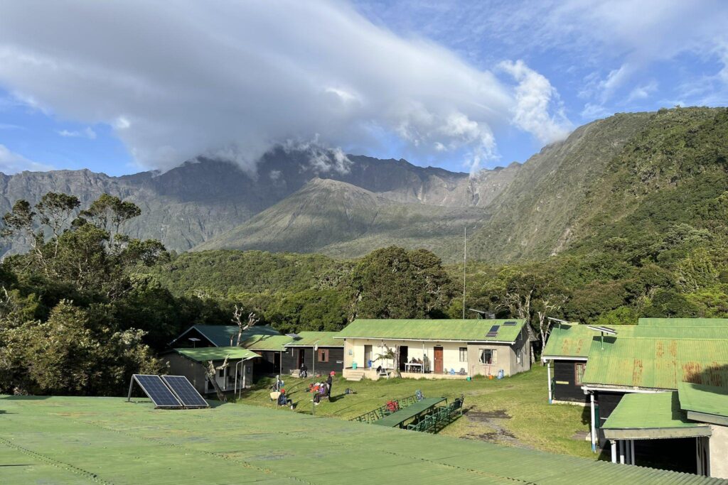 Miriakamba Huts på Mount Meru med grønne tak omkranset av fjell, trær og grønne sletter