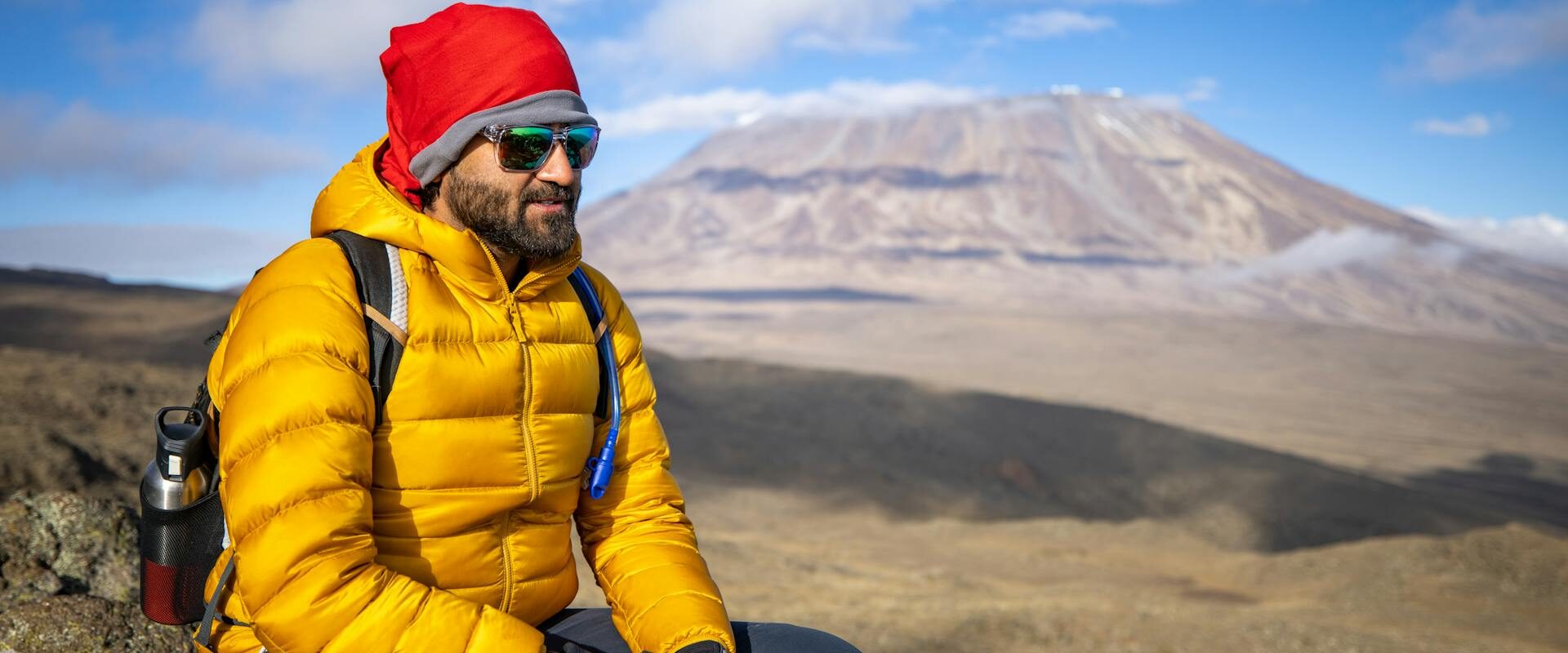 Mann på opplevelsesreise i Tanzania sitter på en sten på vei til Kilimanjaro