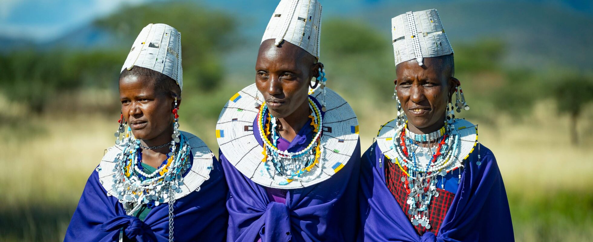 Tre masai-kvinner viser seg i sine tradisjonelle klær på besøk i masailandsby i Tanzania