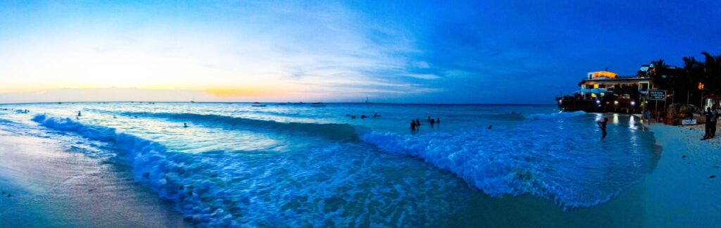 Stranden på Nungwi, Tanzania, i solnedgang med store bølger og mennesker som svømmer i havet