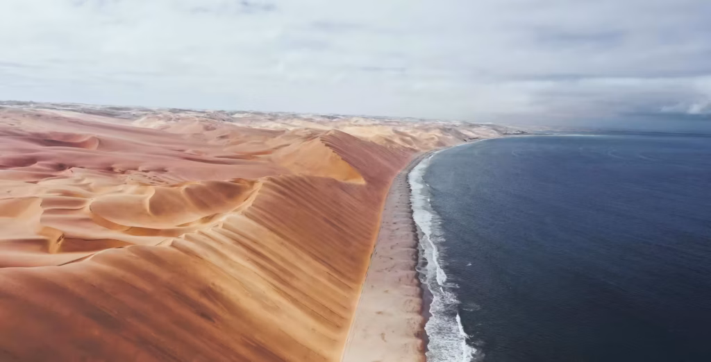 Sandwich Harbour i Namibia sett ovenfra, med høye sanddyner til venstre, en strand i midten og havet til høyre